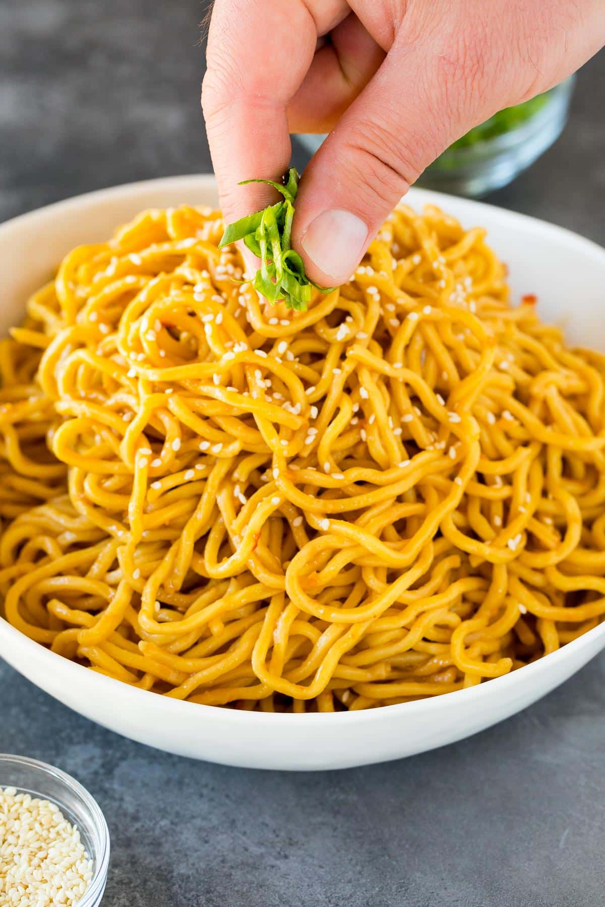 A hand sprinkling green onions over noodles.