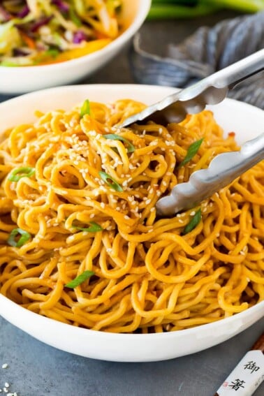 Tongs serving up a portion of sesame noodles.