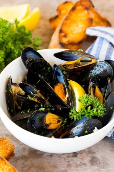 A bowl of steamed mussels served with parsley, lemon and grilled bread.