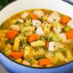 A pot of turkey noodle soup with vegetables, garnished with parsley.