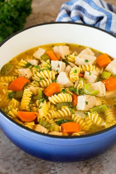 A pot of turkey noodle soup with vegetables, garnished with parsley.