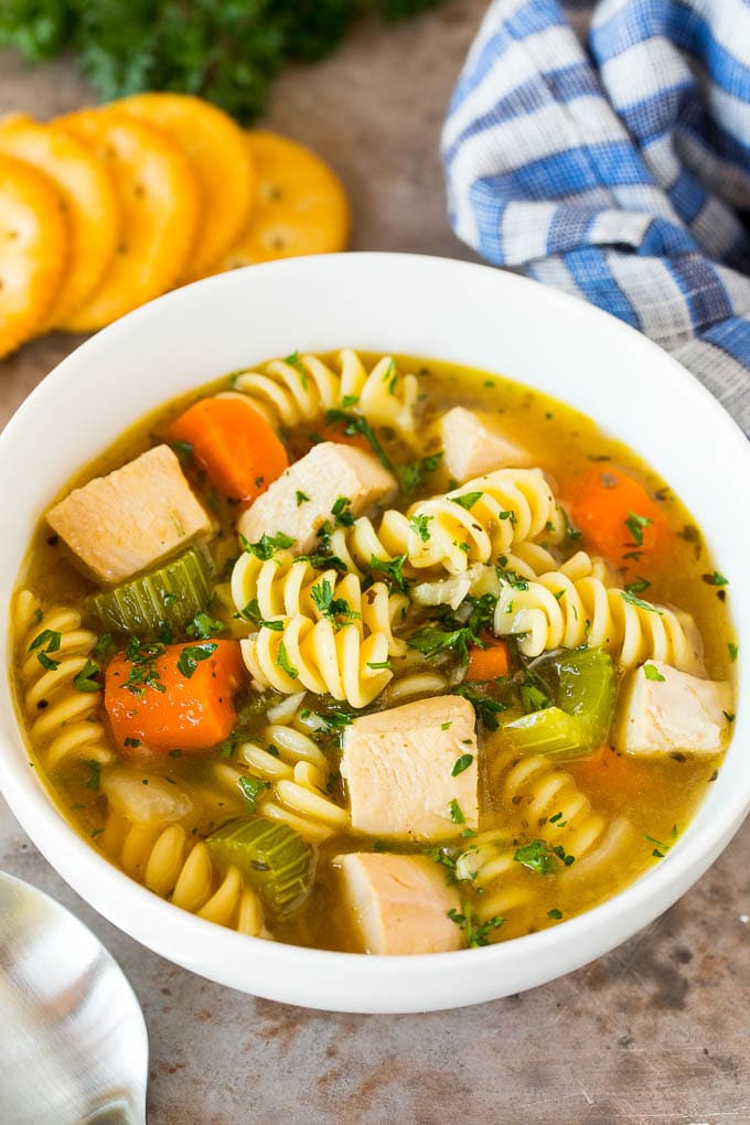 A bowl of turkey noodle soup served with parsley and crackers.