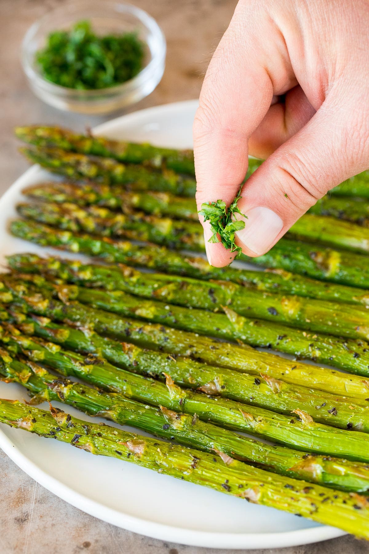 Parsley being sprinkled over a plate of cooked asparagus.