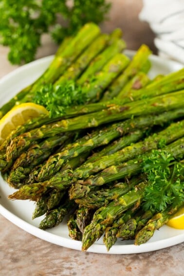 A plate of air fryer asparagus garnished with lemon and parsley.