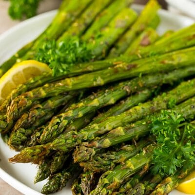 A plate of air fryer asparagus garnished with lemon and parsley.