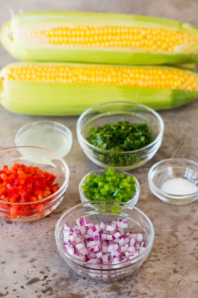 Corn on the cob and bowls of peppers, onions and cilantro.