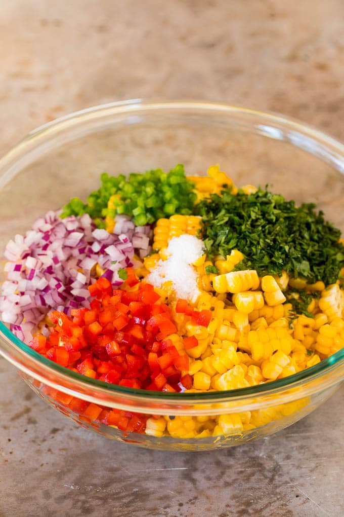 A bowl of corn, vegetables, salt and herbs.