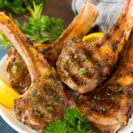 Grilled lamb chops on a plate garnished with parsley and lemon.