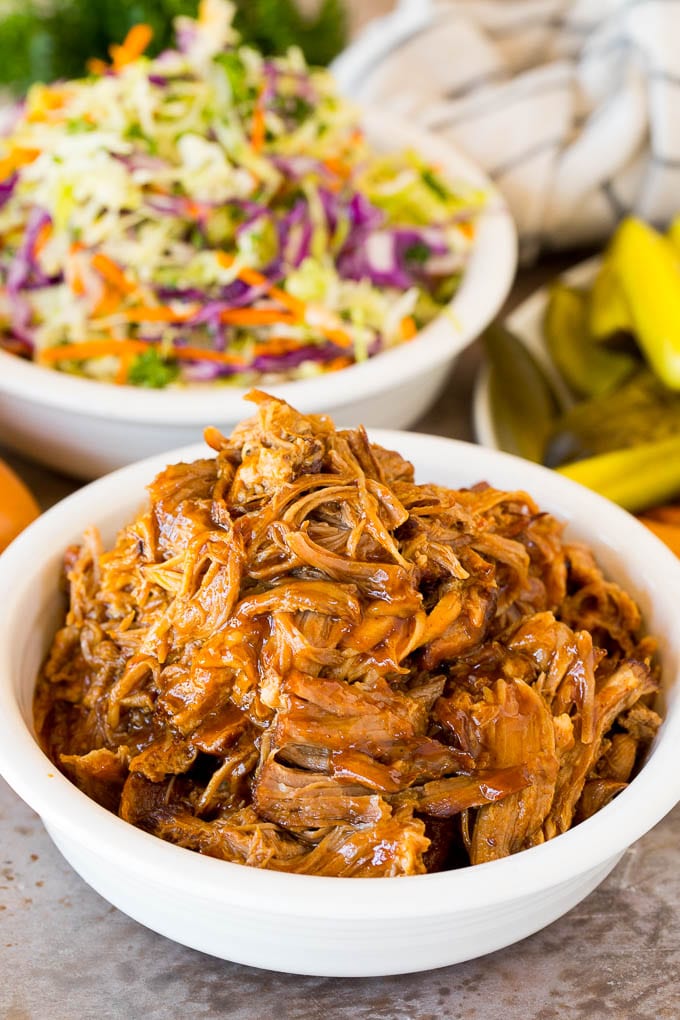 A bowl of Instant Pot pulled pork served with coleslaw and pickles.