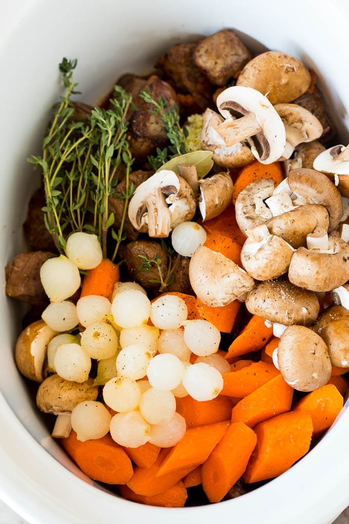 A slow cooker filled with vegetables, browned beef and herbs.