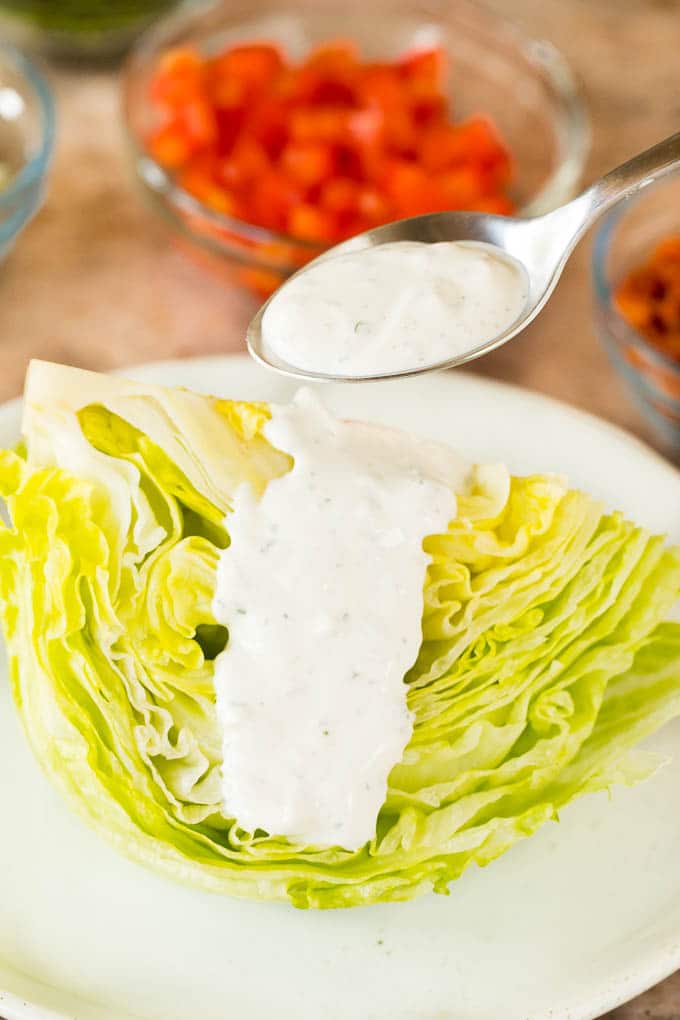 A spoon pouring dressing over a wedge of lettuce.