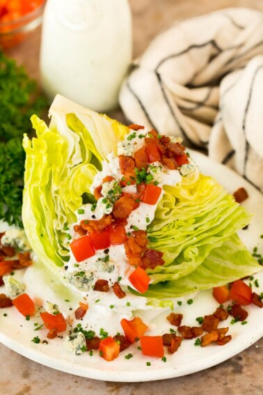 A wedge salad topped with bacon, tomatoes and cheese.