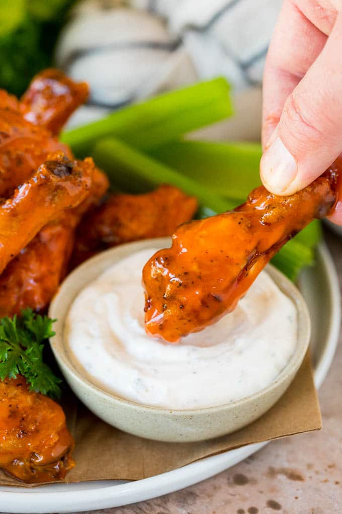 A hand dipping air fryer chicken wings into ranch sauce.