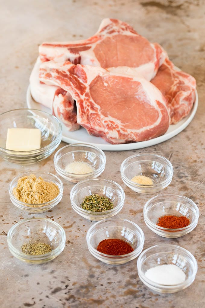 Pork chops on a plate with bowls of herbs and spices.