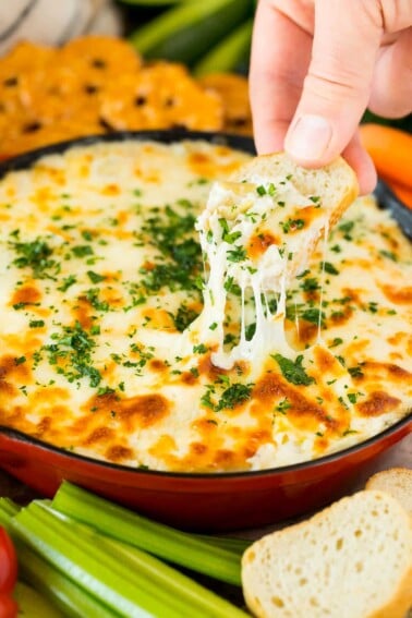 A hand putting a piece of bread into artichoke dip.