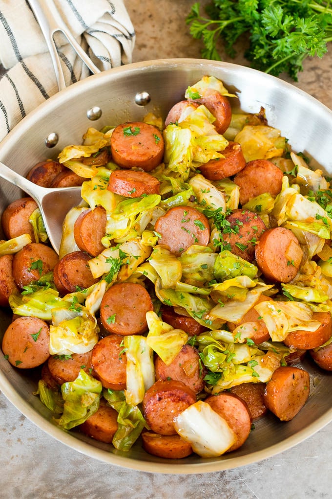 A pan of cabbage and sausage with parsley and a serving spoon.