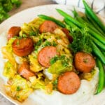A plate of cabbage and sausage served over mashed potatoes with green beans.