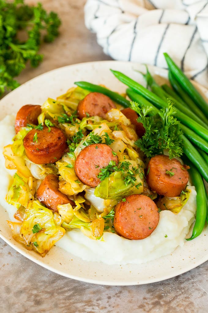 A plate of cabbage and sausage served over mashed potatoes with green beans.