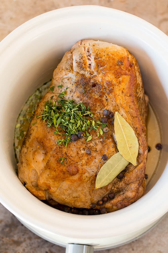 Pork in a slow cooker with chicken broth, bay leaves, thyme and juniper.