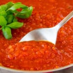 A serving spoon in a pan of homemade marinara sauce.