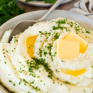 A bowl of make ahead mashed potatoes topped with butter and herbs.