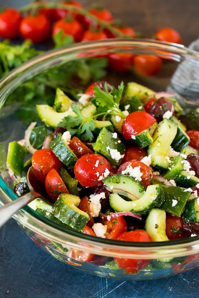 A spoon in a bowl of Mediterranean salad that is garnished with feta cheese.