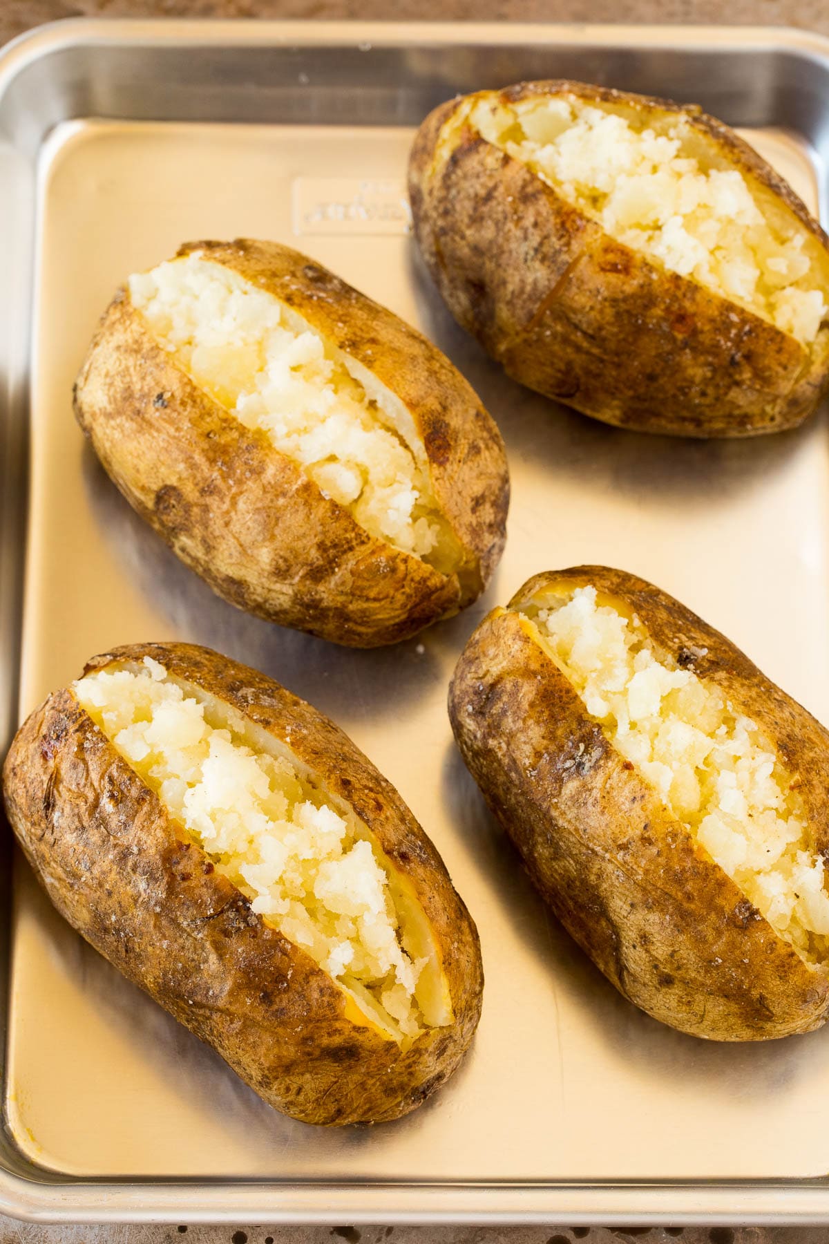 Cooked potatoes split open on a sheet pan.