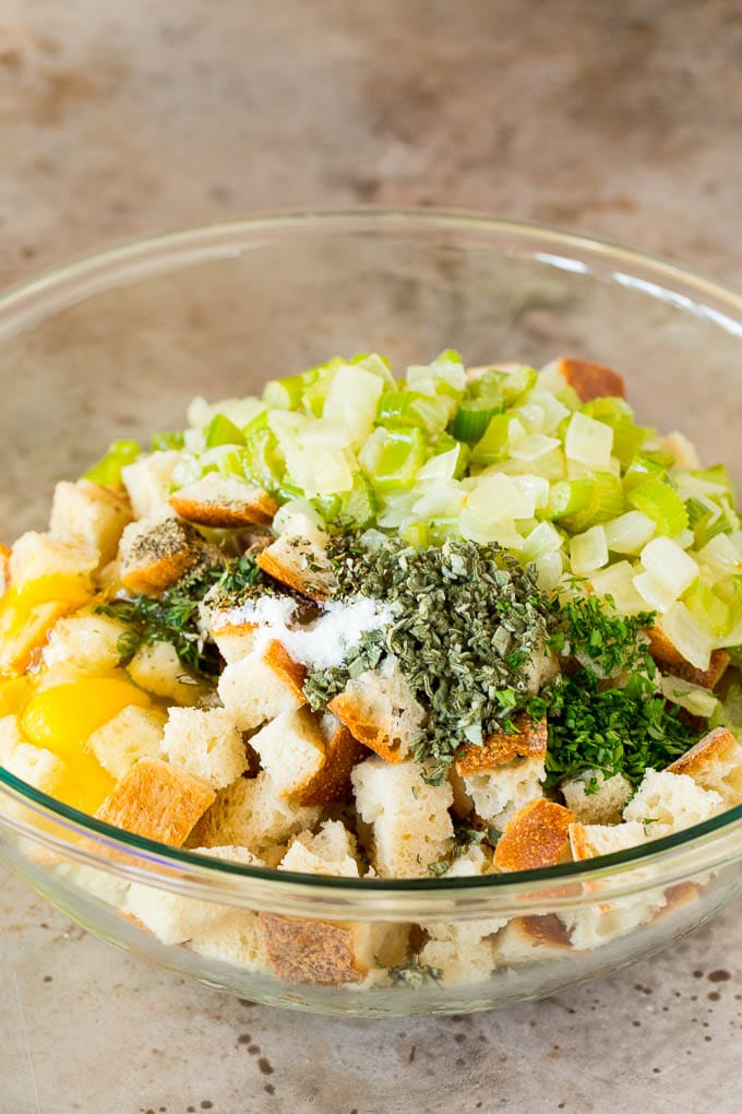 This Thanksgiving stuffing is a mixture of bread cubes, vegetables and plenty of herbs, all baked together until golden brown. A bowl of bread cubes with eggs, bread and vegetables.