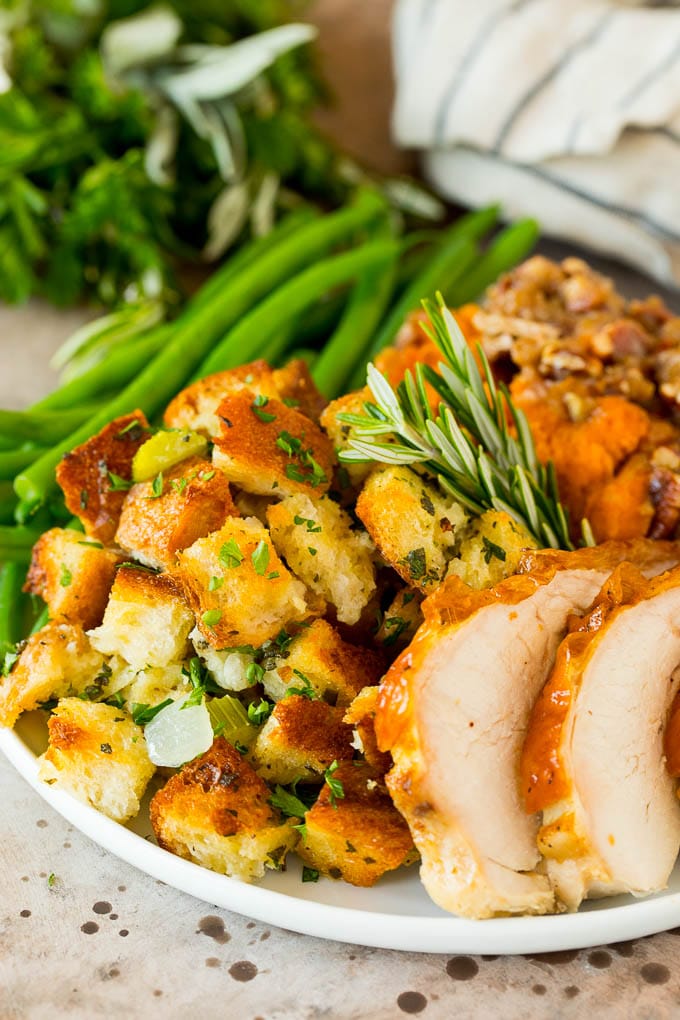 This Thanksgiving stuffing is a mixture of bread cubes, vegetables and plenty of herbs, all baked together until golden brown. Thanksgiving stuffing on a plate with sweet potatoes, turkey and green beans.