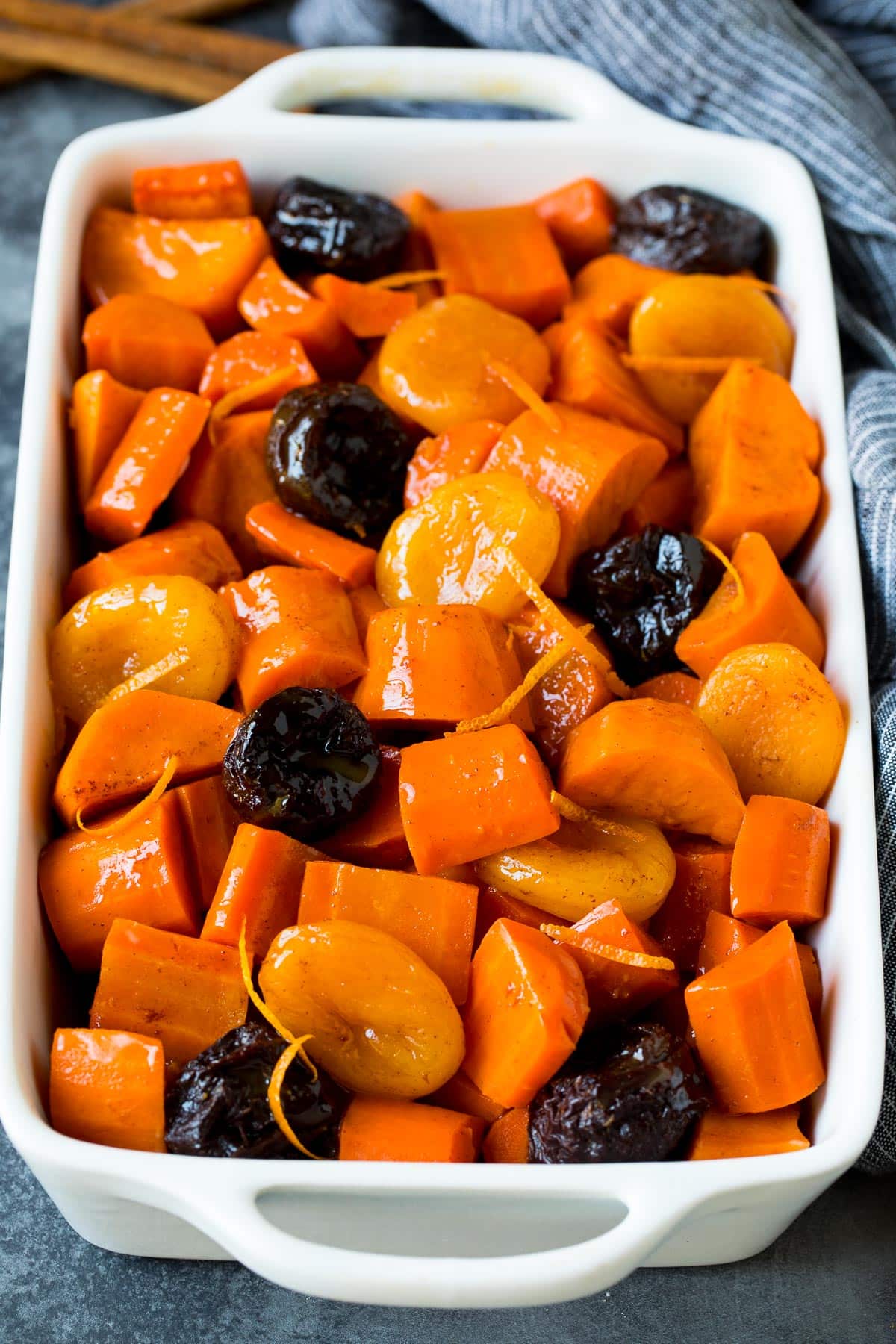 A casserole dish full of tzimmes that is garnished with orange zest.