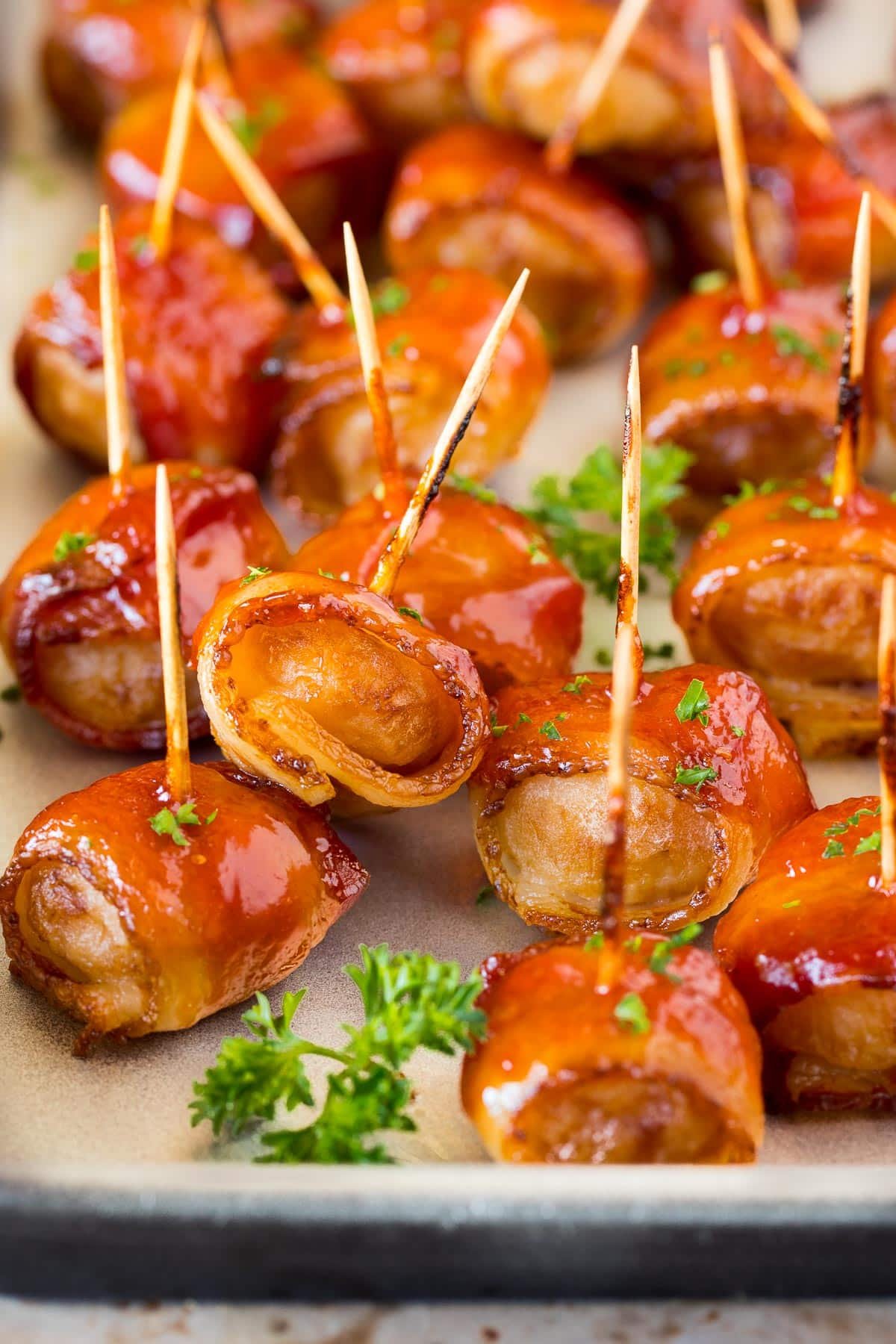 Bacon wrapped water chestnuts on a sheet pan, garnished with parsley.