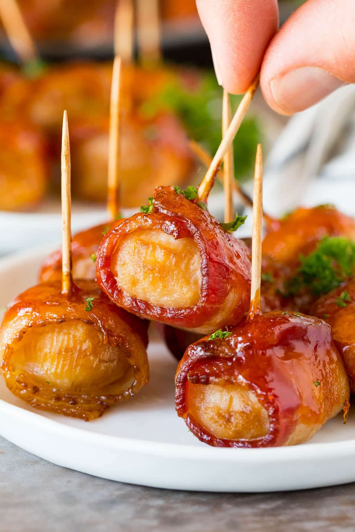 A hand taking bacon wrapped water chestnuts off a serving plate.