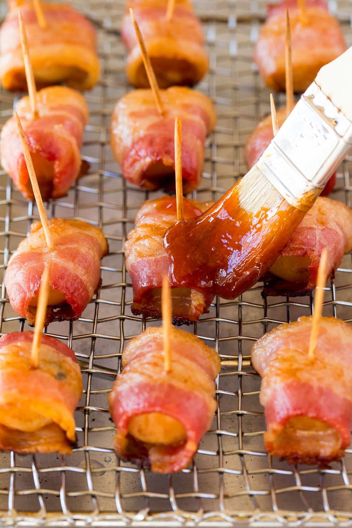 Sauce being brushed over water chestnuts that are coated in bacon.