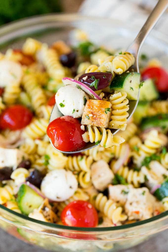 A spoon holding up a serving of chicken pasta salad.