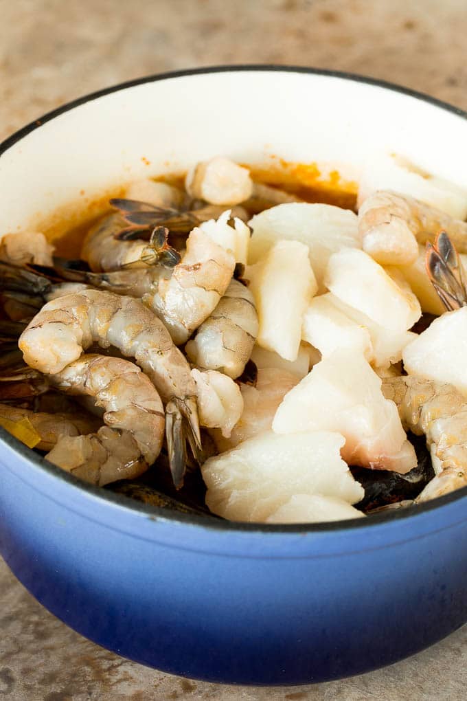 A pot with broth, fish and shrimp in it.