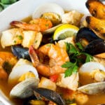 A serving bowl of bouillabaisse with shrimp, clams and fish.