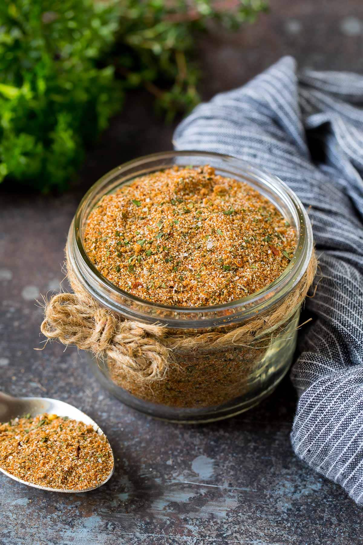 A jar of Jamaican jerk seasoning surrounded by fresh herbs.