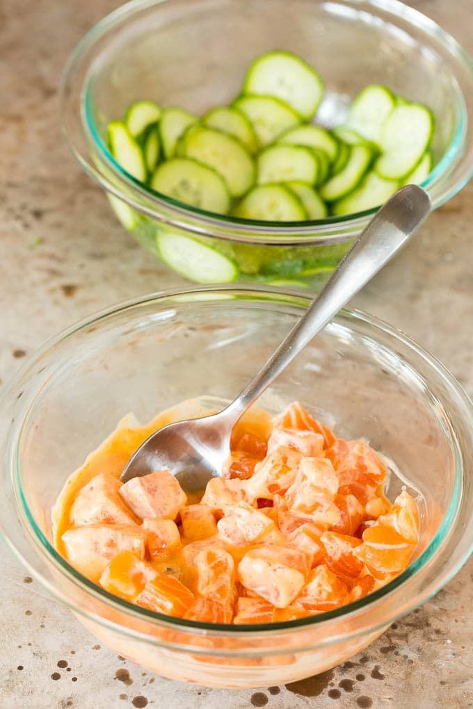 Bowls of marinated cucumbers and salmon in spicy mayo.
