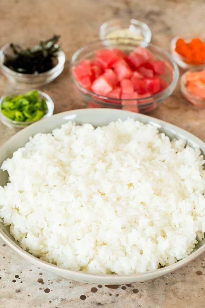 A bowl of sushi rice with bowls of toppings around it.