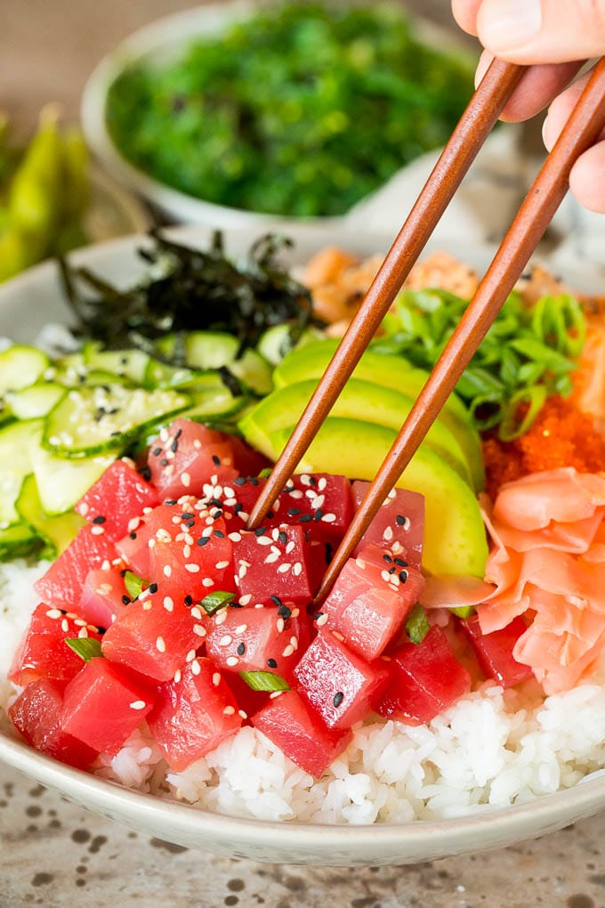 Chopsticks picking up a piece of ahi tuna in a sushi bowl.