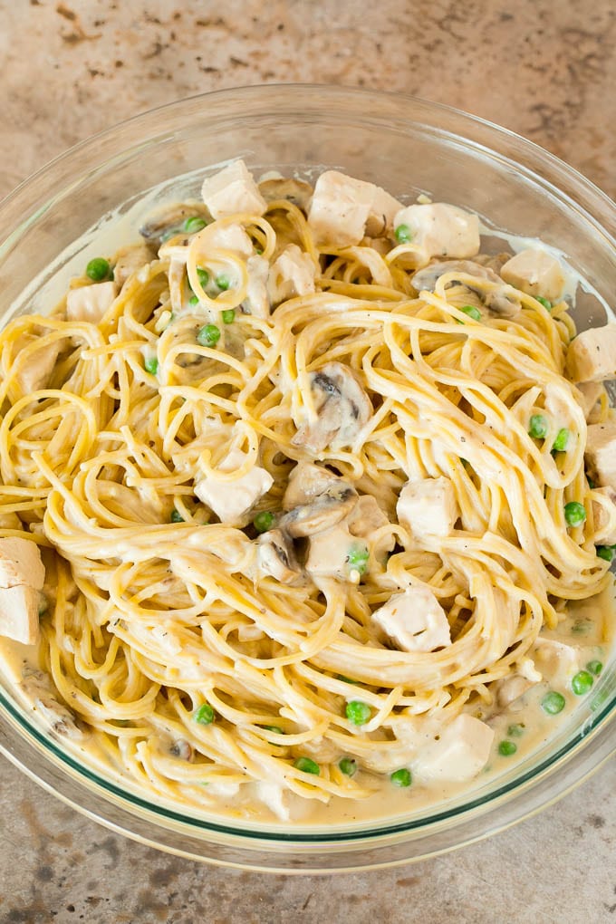 A mixing bowl of pasta, peas and turkey, all tossed in a creamy sauce.