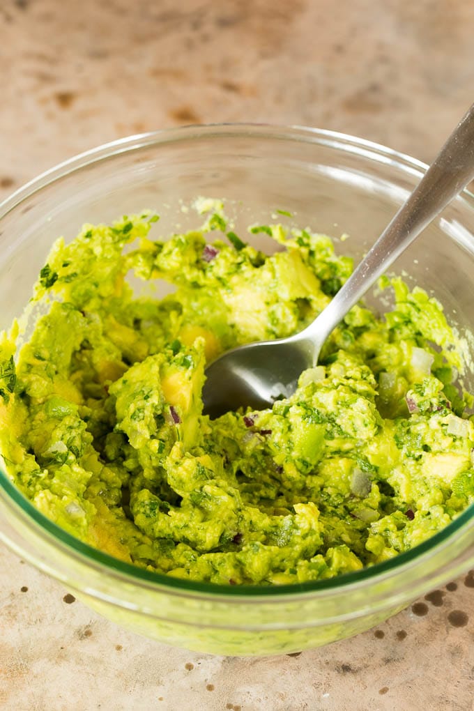 A bowl of avocado stirred together with seasonings.