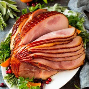 A spiral ham coated in glaze, garnished with fruit and herbs.