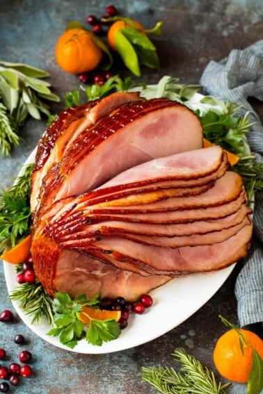A spiral ham coated in glaze, garnished with fruit and herbs.