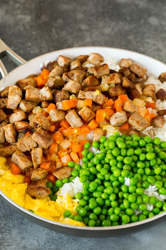 A pan with cooked rice, peas, carrots, pork and eggs.