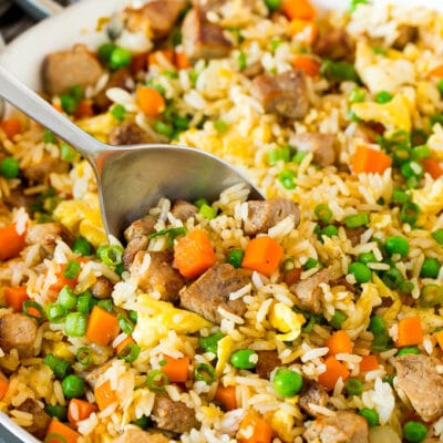 A pan of pork fried rice with a serving spoon in it.