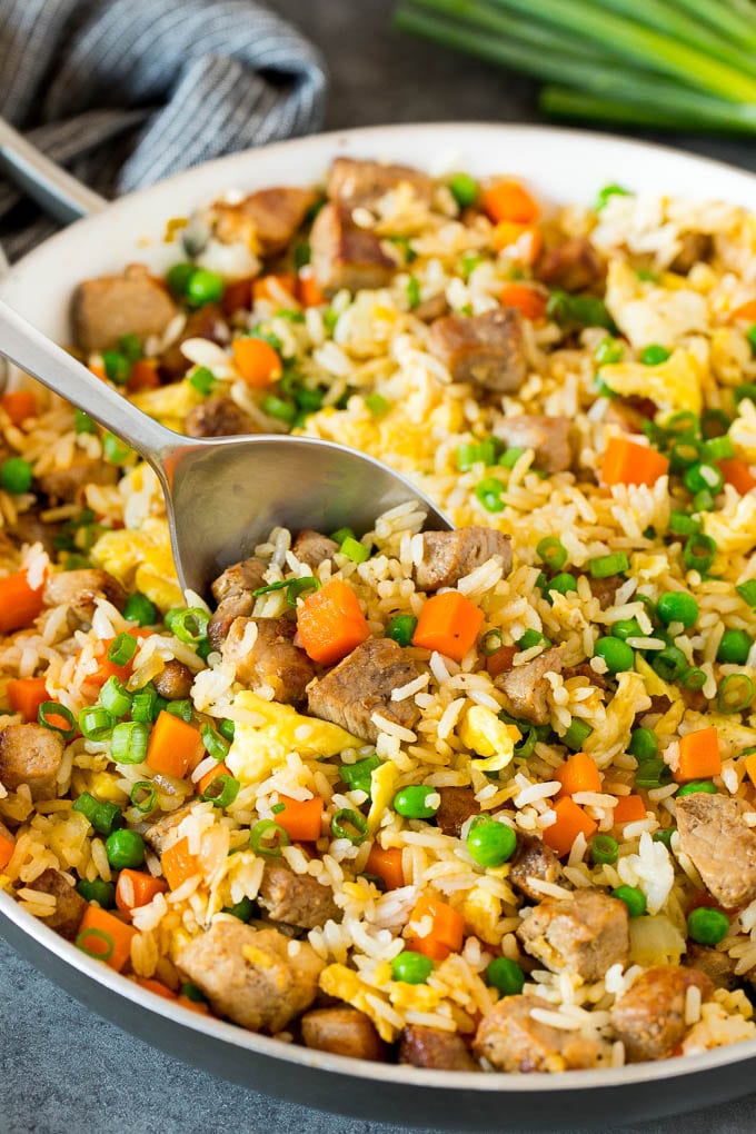 A pan of pork fried rice with a serving spoon in it.