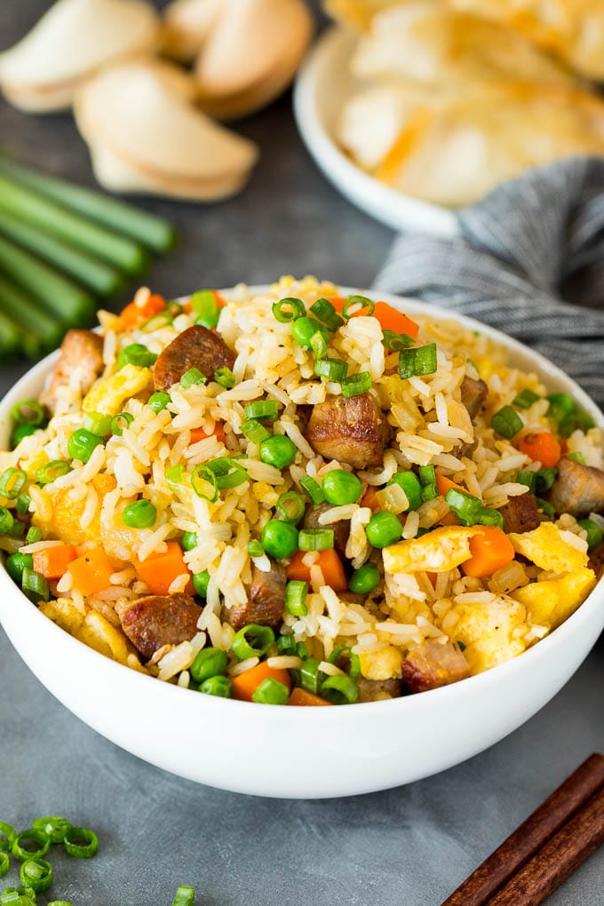 A bowl of pork fried rice with vegetables in it.