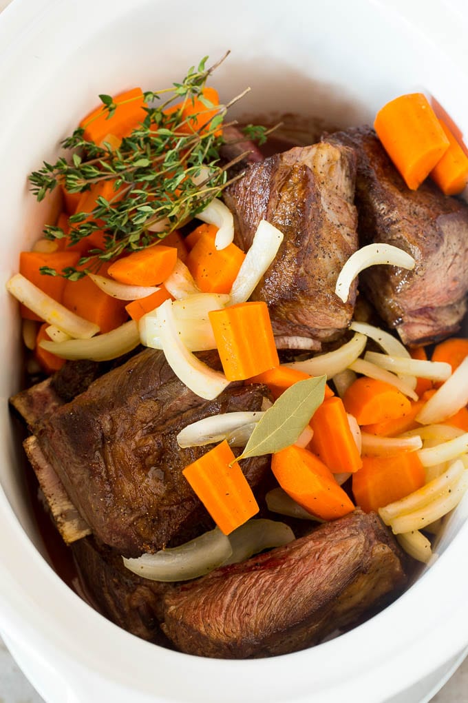 Short ribs in a slow cooker with sauce, carrots and herbs.
