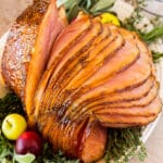 A glazed Easter ham on a platter garnished with herbs and apples.